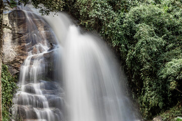 The natural background of a waterfall flowing from a height through rocks and various trees. The...
