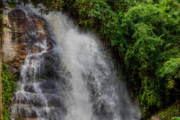 The natural background of a waterfall flowing from a height through rocks and various trees. The...