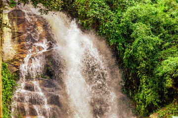 The natural background of a waterfall flowing from a height through rocks and various trees. The...