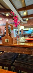 Rustic wooden table in a restaurant with cutlery, red plates and a wooden spice rack. Pink flowers decorate the center of the table. Natural lighting and wooden ceiling with exposed beams