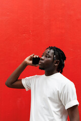 African man with dreadlocks hairstyle talking on the phone standing at red background