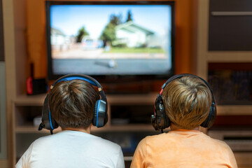 Two children with headphones on their backs, in front of a television in their living room. Concept of video game