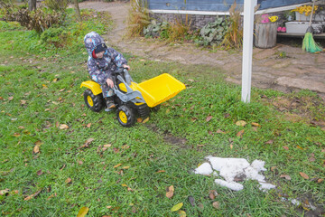 a child boy on a wheeled bulldozer tractor removes snow with a snow plow, photo without filters