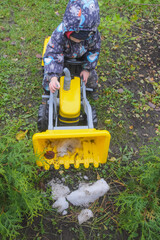 a child boy on a wheeled bulldozer tractor removes snow with a snow plow, photo without filters