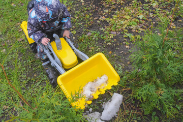 a child boy on a wheeled bulldozer tractor removes snow with a snow plow, photo without filters
