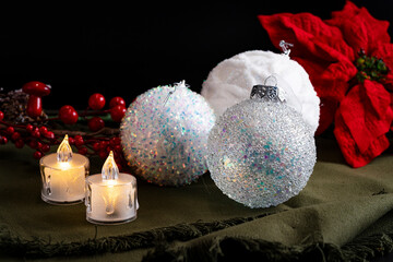 Candles and white christmas balls on green fabrics with red flowers and berries