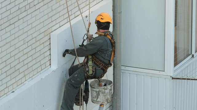 Builder working at height while holding on a rope and insurance. Climber are working on the insulation of facades of a multi-storey residential building.