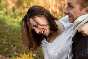 A young couple having fun in an autumn park, a girl with a bouquet of yellow autumn leaves is laughing sincerely.