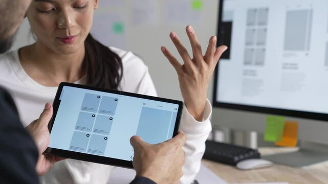 UX UI designer testing prototype on a tablet, discussing and brainstorming on wireframes for a website and mobile app prototype, in the concept of website and mobile application design concept.