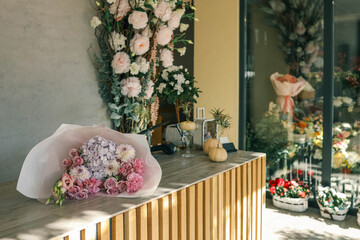 Elegant bouquet of pink roses, hydrangeas, and delicate flowers wrapped in soft paper placed on a wooden counter in a flower shop with warm natural light