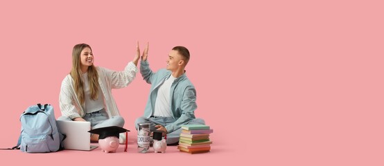 Young students with piggy banks giving each other high-five on pink background with space for text....