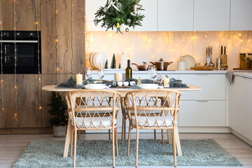 Interior of modern kitchen with festive table setting, glowing lights and Christmas decorations