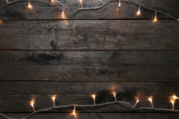 Frame made of glowing Christmas lights on dark wooden background
