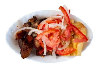 On wooden table there is plate with fried pork and traditional Latin American side dish - fried cassava. Tapita dish is garnished with salad of fresh tomatoes and onions. Isolated over white