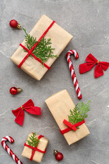 Gift boxes with coniferous branches, Christmas balls, bows and candy canes on grey background