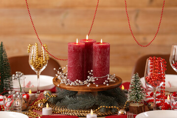 Christmas table setting with burning candles and beads in room, closeup