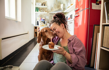 Woman celebrating dogs birthday with a cupcake and party hat in the kitchen