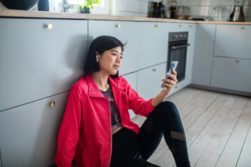 Asian woman using smartphone in kitchen after home workout