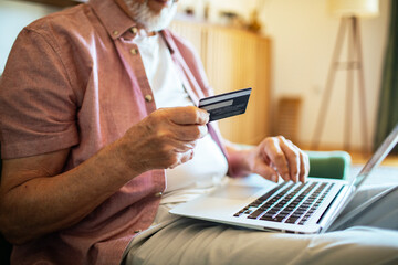 Senior man online shopping with laptop on couch at home