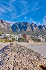 Landscape, rock and beach with buildings, city and sky with mountain view, outdoor and summer in nature. Stone, boulder and environment with sand, hill and urban expansion on horizon in South Africa