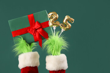 Hairy creature in Santa costume with Christmas gift box and figure 25 made of balloons on green...