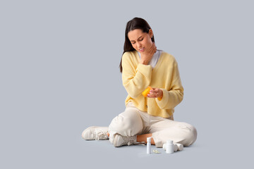 Young woman with pills and spray for sore throat sitting on grey background
