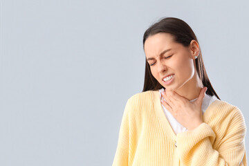 Young woman suffering from sore throat on grey background