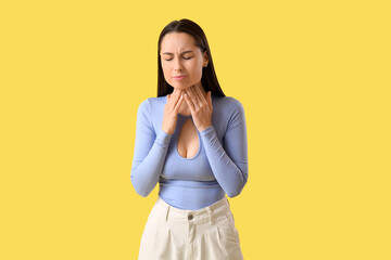 Young woman suffering from sore throat on yellow background