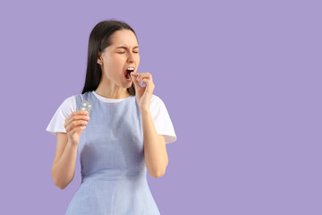 Young woman with pills for sore throat on lilac background