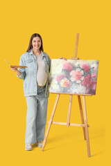 Naklejka premium Beautiful female pregnant artist painting on canvas on yellow background