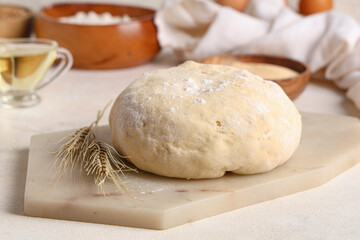 Board with fresh raw dough and wheat on white background