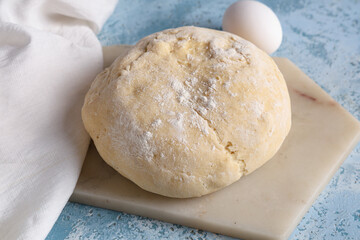 Board with fresh raw dough and egg on blue background