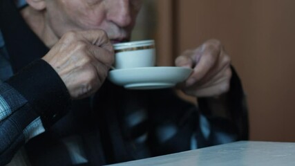 Caucasian elderly man 70 -79 years old drinks coffee from a cup while inside, pensioner has breakfast drinking a cup of aromatic coffee