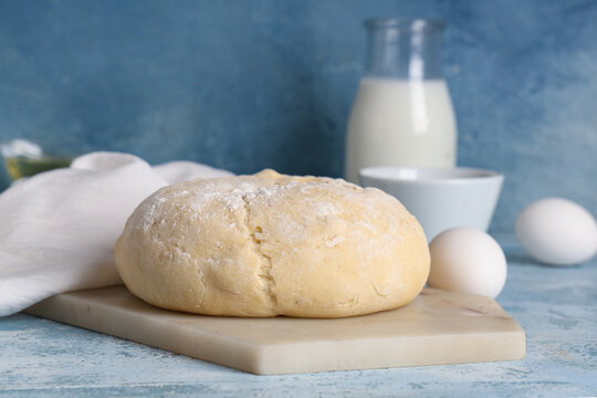 Board with fresh raw dough and eggs on blue background