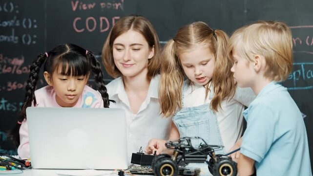 Caucasian teacher using laptop and explain about engineering system while diverse student holding electronic equipment in front of blackboard with prompt or code written in STEM class. Erudition.