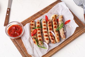 Wooden board with tasty grilled sausages and glass bowl of sauce on white background