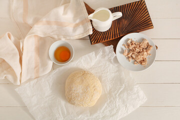 Baking paper with fresh dough, yeast, raw egg and jug of milk on white wooden background