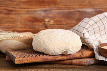 Board with fresh raw dough and wheat on wooden background