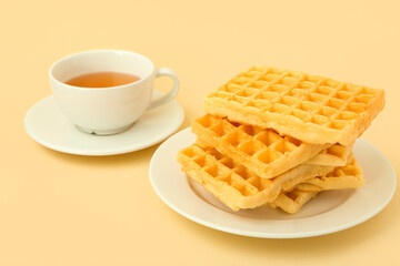 Delicious Belgian waffles in plate with cup of tea on yellow background
