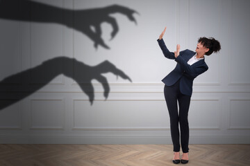 Businesswoman scared by hands of monster reaching for her. Creepy shadow on white wall