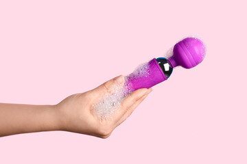 Woman washing purple vibrator on pink background, closeup