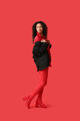 Beautiful young African-American woman in stylish red tights on color background