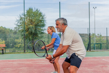 lateral view of senior tennis couple holding rackets ready to play during match