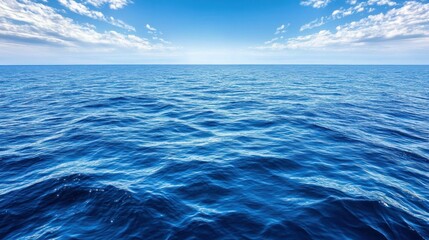 Obraz premium A vast, blue ocean stretching out to the horizon with a bright blue sky and white puffy clouds.