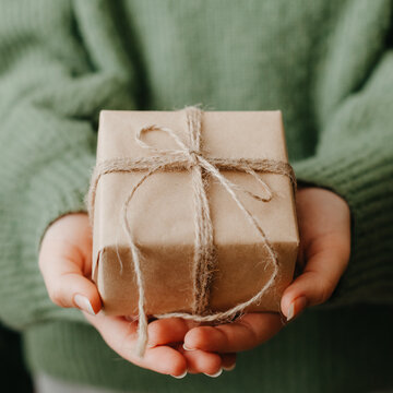 Woman in a green sweater showcasing a sustainable and heartfelt christmas gift wrapped in simple brown paper and twine
