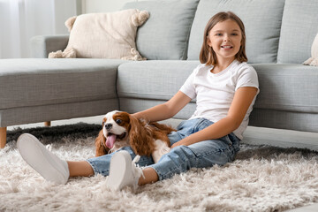 Cute little girl with King Charles spaniel dog sitting on carpet in living room