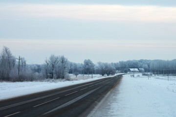 Road infrastructure. Panoramic view of the winter highway going away in the distance among the picturesque frosted trees and huts in the distance. Copy space.