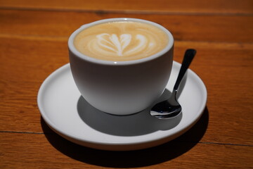 A beautifully crafted cup of latte art on a wooden table with a spoon beside it, showcasing morning coffee elegance in a cozy cafe setting