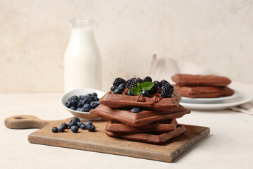 Wooden board of sweet chocolate Belgian waffles with fresh blueberries and blackberries on white background
