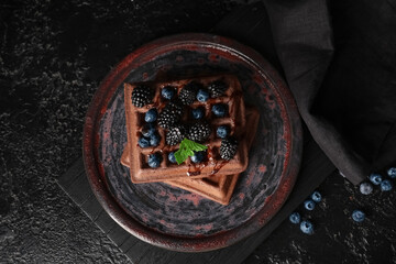 Plate of sweet chocolate Belgian waffles with fresh blackberries and blueberries on black background